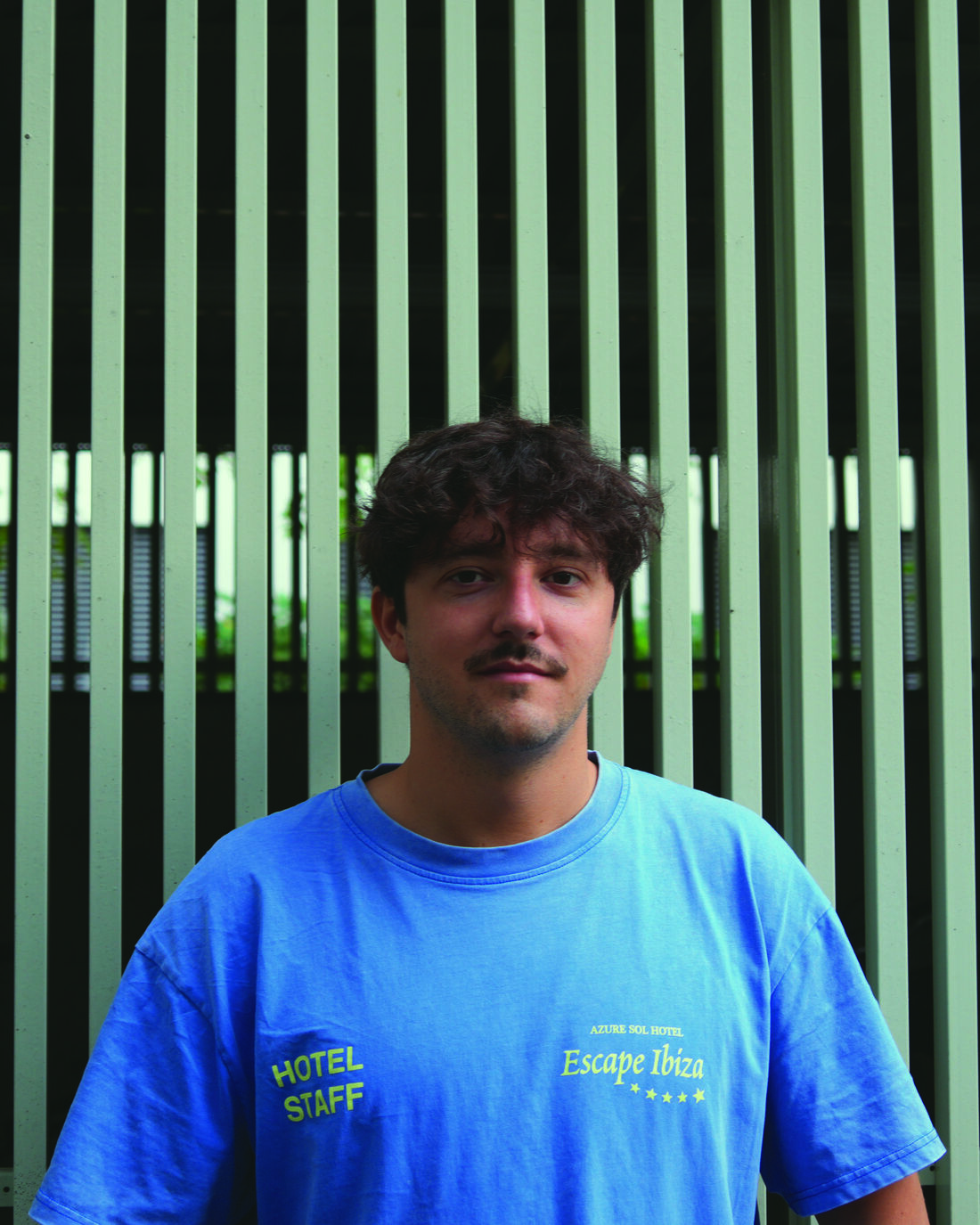 SIL im blauen T-Shirt vor einer grünen Lamellenfassade